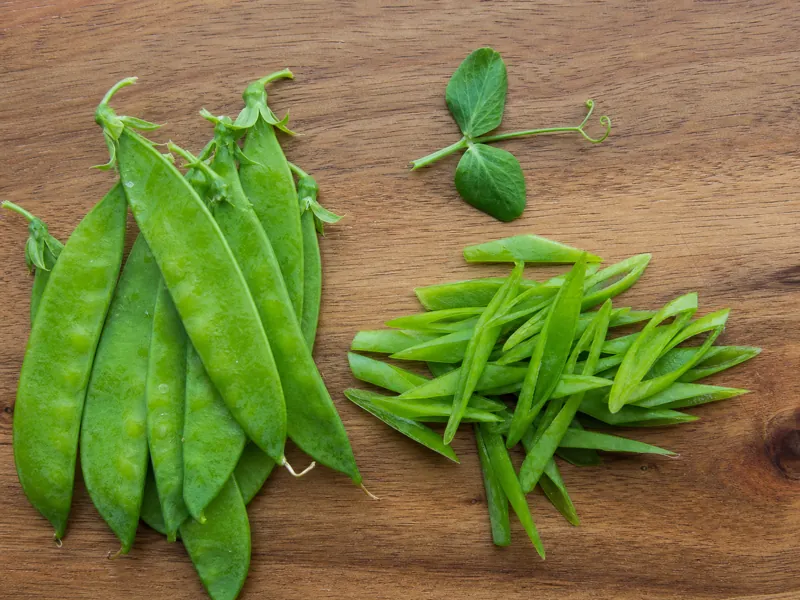 Snow peas sliced thinly beside a pea shoot sprig | EpicureDelight