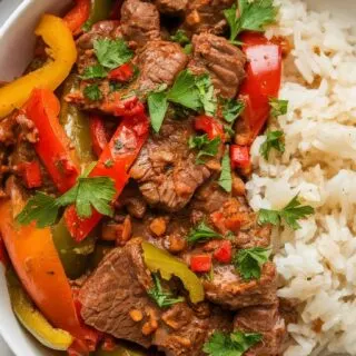 Top-down image of Spicy Cajun Beef Stir-Fry plated on a white marble counter. The juicy beef is coated in a bold Cajun sauce, tossed with sautéed bell peppers and onions. Garnished with parsley and red pepper flakes, this quick and easy stir-fry is perfect for a flavorful weeknight meal.