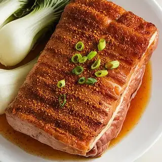 Crispy five-spice pork belly fresh from the oven, its skin golden and blistered. The rich layers of fat and meat are perfectly roasted, ready to be sliced and served.