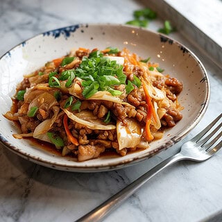 A photograph of a serving of egg roll stir fry in a white ceramic dish, garnished with finely chopped green onions. The stir fry is a mix of ground pork, shredded cabbage, and finely diced carrots, all coated in a rich savory sauce, placed on a white ceramic plate. The plate rests on a sleek marble countertop, with a polished silver fork positioned to the right, ready for serving. Soft, natural light from a nearby window casts a gentle glow, highlighting the colors and textures of the dish.