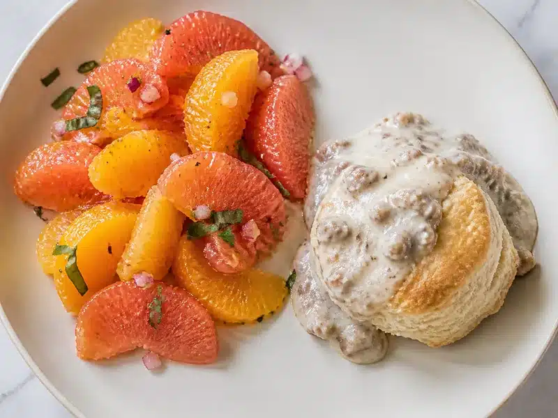 Fresh citrus salad beside biscuits and sausage gravy - breakfast side | EpicureDelight